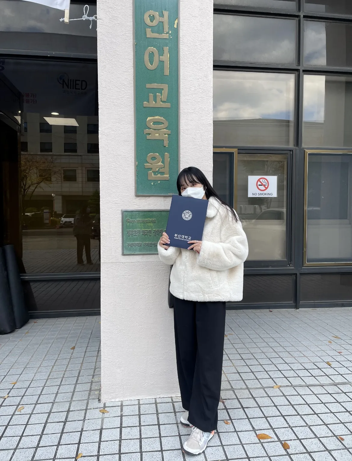 語学学校の建物の前で修了証書を持つりんさん